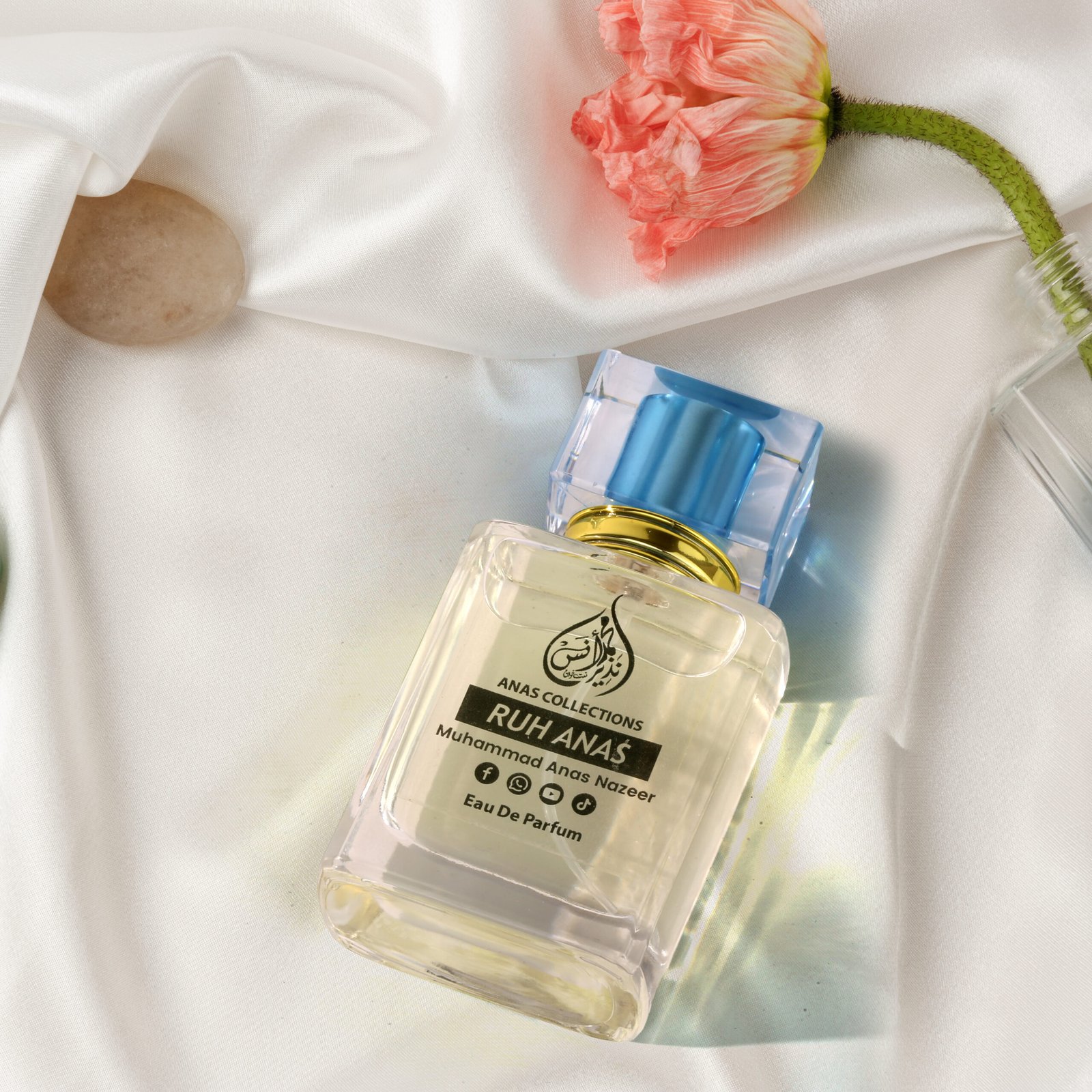 Luxury Ruh Anas perfume bottle styled on white silk with a pink flower.